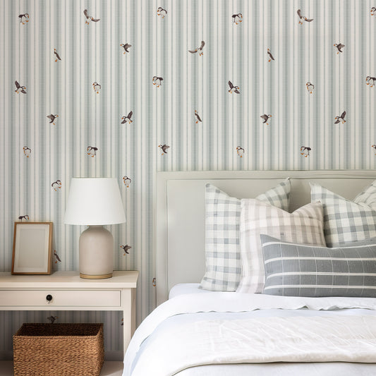 Bedroom with striped wallpaper, bed with plaid pillows, and side table with lamp.
