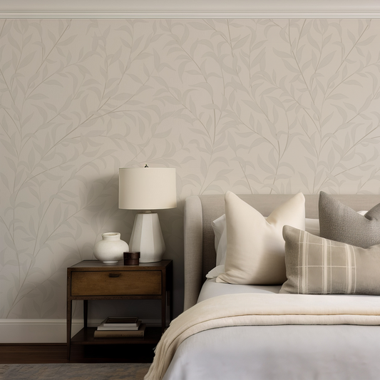 Neatly made bed with pillows against a wall with leaf-patterned wallpaper.