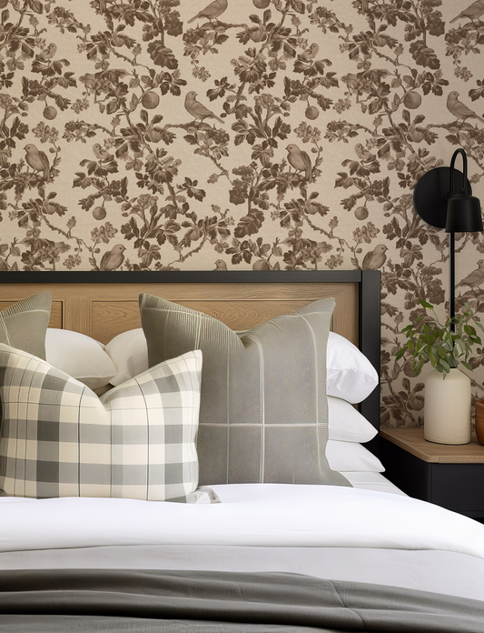 Bedroom with floral wallpaper, bed with plaid and solid pillows, and nightstand with lamp.