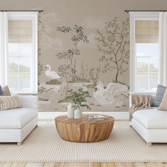 A styled living room featuring a large wall mural with a classic French Chinoiserie design of white swans, bamboo, and trees on a beige background. The room is furnished with a round wooden coffee table, white sofas, and neutral-toned decor.