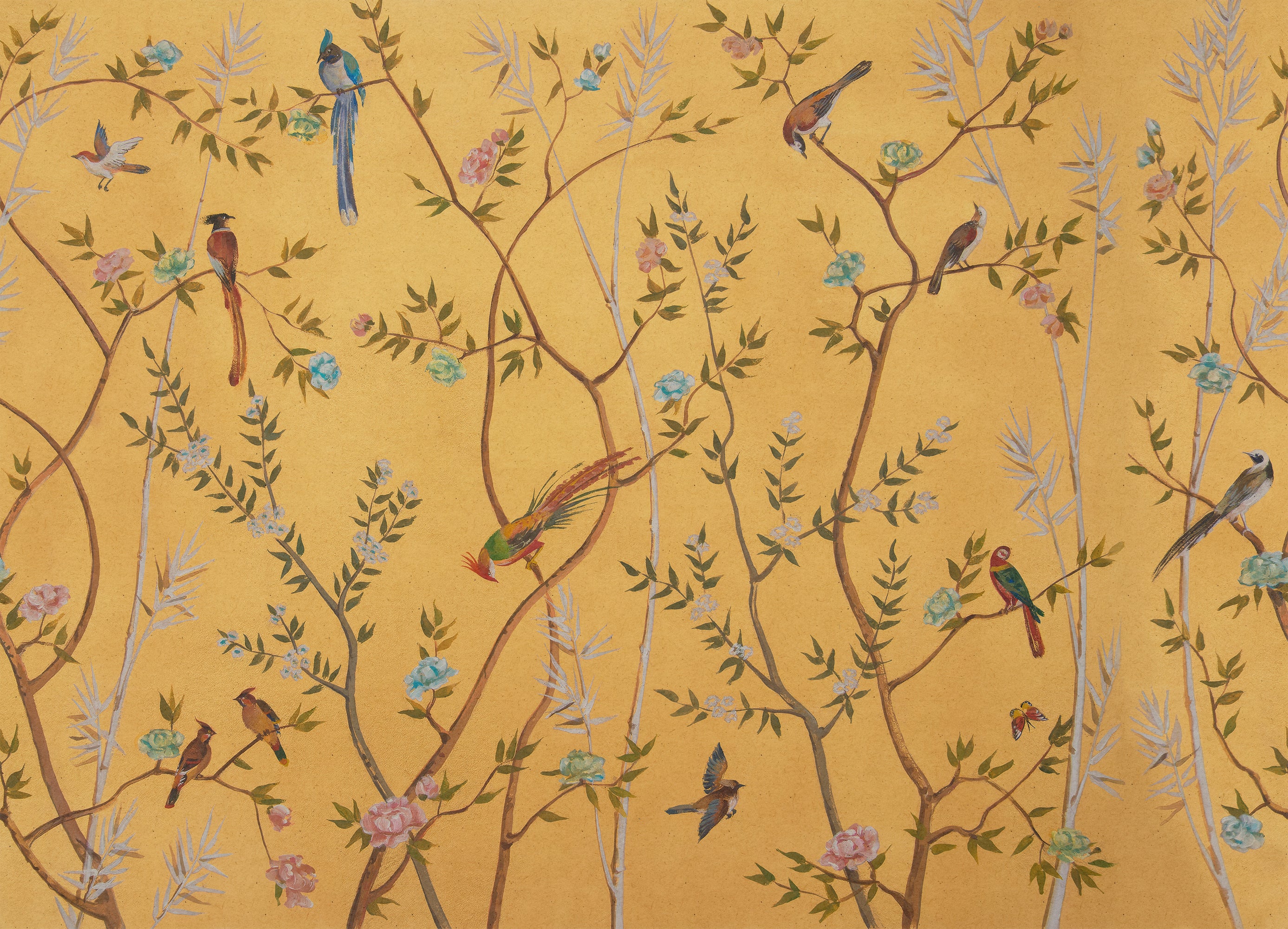 A close-up of a decorative wallpaper or fabric pattern featuring a warm mustard yellow background with delicate branching vines, small leaves, pink and blue flowers, and numerous birds in blue, green, brown, and red tones.